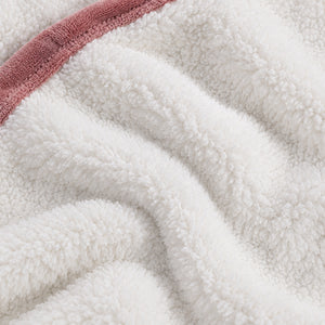Close-up of a plush white sherpa or fleece fabric with soft folds and a dusty rose pink terry trim along the edge.