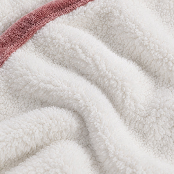 Close-up of a plush white sherpa or fleece fabric with soft folds and a dusty rose pink terry trim along the edge.