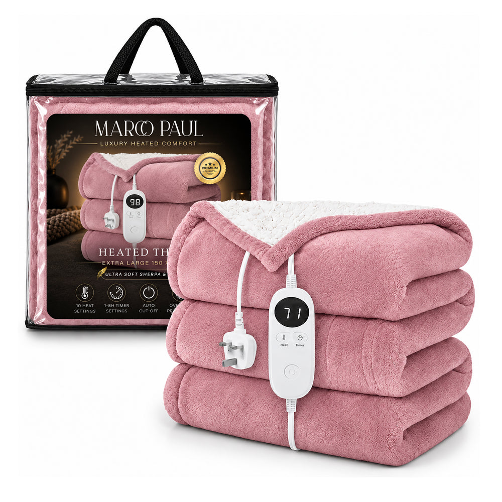 A pink heated blanket with a white sherpa lining draped over a beige sofa in a cozy living room setting. The blanket features a ribbed texture and a white control panel with a cord is attached.