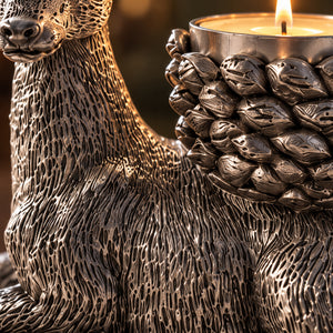Close-up of a metallic bear-shaped candle holder with a lit tealight candle, showing detailed textured carving and a warm glowing flame against a dark blurred background.