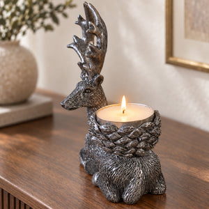 A deer-shaped candle holder with a lit tea light candle, displayed on a wooden table in a warm indoor setting.