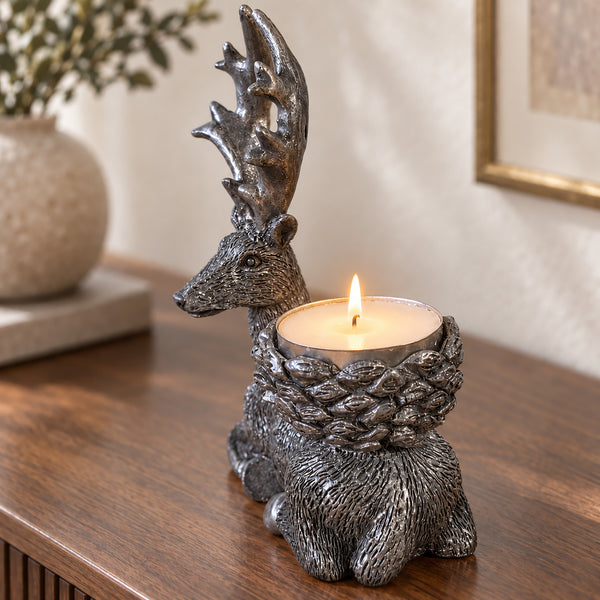 A deer-shaped candle holder with a lit tea light candle, displayed on a wooden table in a warm indoor setting.