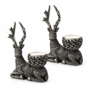 Two deer-shaped candle holders with textured antlers and pinecone-embossed backs, each holding a white tea light, photographed on a clean white background.