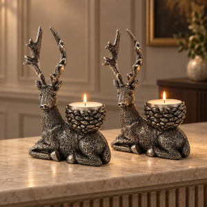 Two deer-shaped candle holders with pinecone-style cups, each holding a lit tealight candle, displayed on a marble countertop in a warm, elegant interior setting.