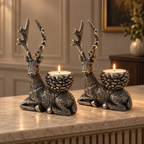 Two deer-shaped candle holders with pinecone-style cups, each holding a lit tealight candle, displayed on a marble countertop in a warm, elegant interior setting.