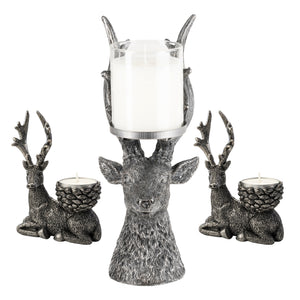 Three deer-shaped candle holders in a textured silver finish, including one large deer head holding a white pillar candle and two smaller seated deer holding tea light candles, shown on a white background.