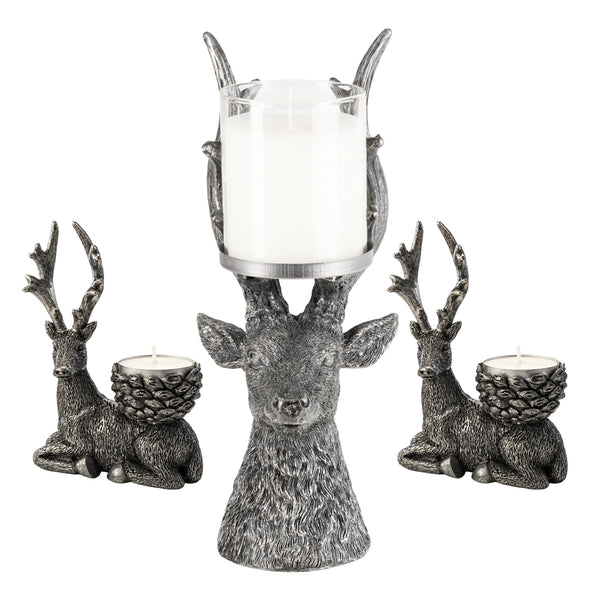 Three deer-shaped candle holders in a textured silver finish, including one large deer head holding a white pillar candle and two smaller seated deer holding tea light candles, shown on a white background.