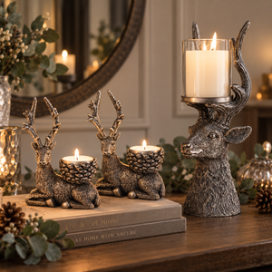 A set of rustic deer-shaped candle holders with pinecone centers and antler-shaped holders, styled on a wooden table with a book and greenery in a cozy indoor setting.