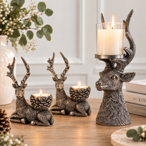 Three deer-shaped candle holders with pinecone-style cup holders are arranged on a wooden table. Two are unlit and one is lit with a white pillar candle.