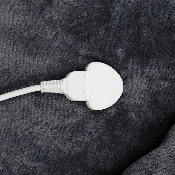A close-up of a white electrical plug connected to a white cable, resting on a dark gray plush fabric surface.