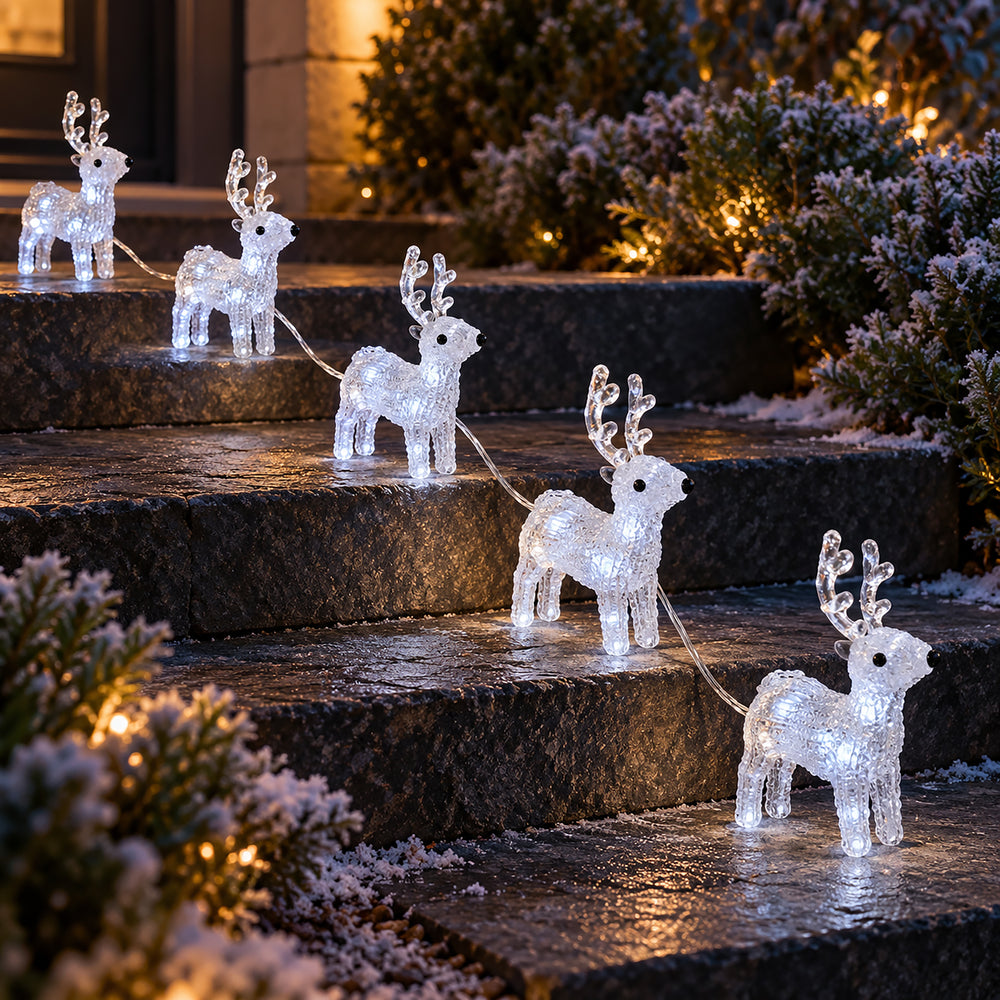 Five illuminated crystal reindeer yard lights arranged on outdoor stone steps at night, with warm lights and snowy greenery in the background.