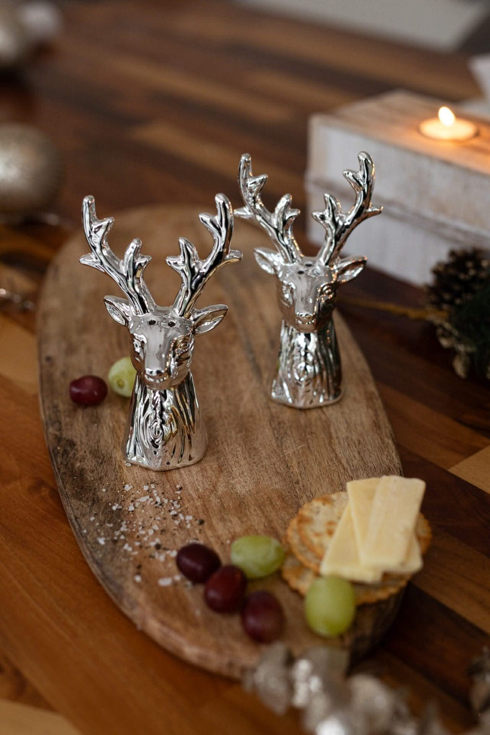 A pair of silver salt and pepper shakers designed to resemble stag heads, placed on a wooden table.