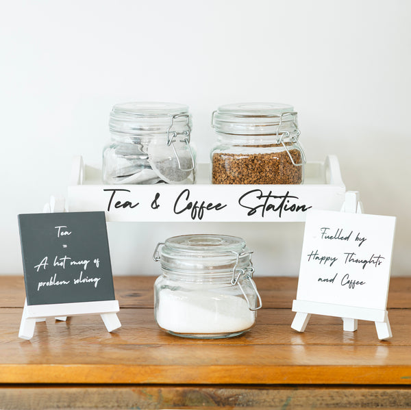 Tea and coffee station with jars and small signs on a wooden surface.