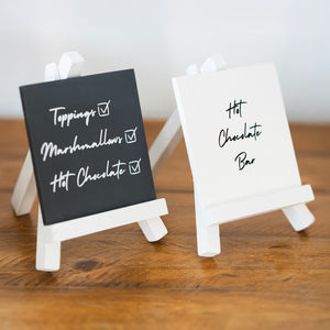 Two small easel signs on a wooden surface, one black with white text and the other white with black text.
