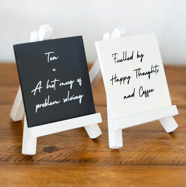 Two small easel signs with humorous text on a wooden surface.