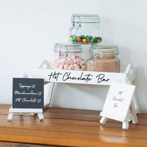 Hot chocolate bar setup with jars of toppings on a wooden surface.