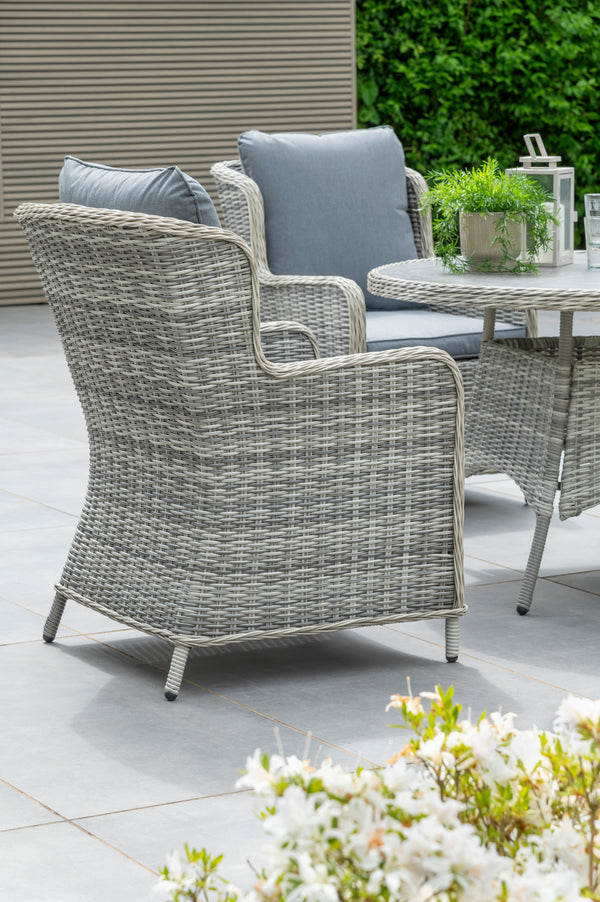 Outdoor patio furniture set with wicker chairs and a glass table on a patio.