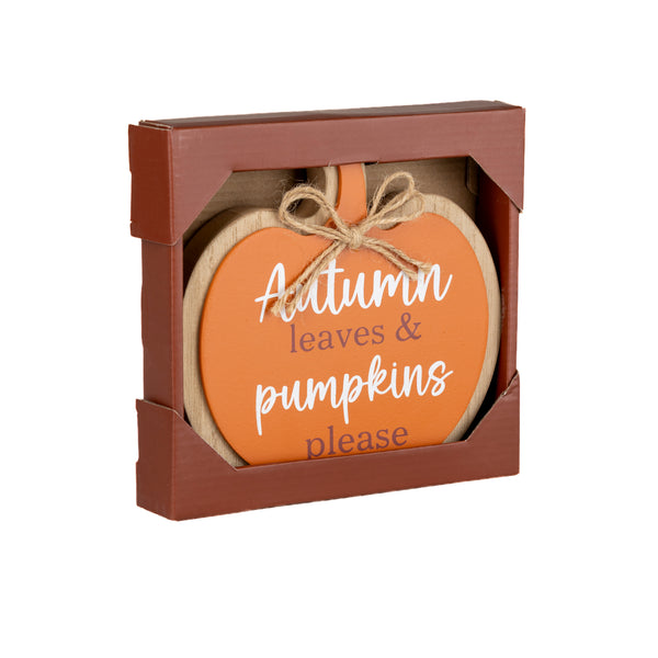 An autumn-themed wooden sign in a brown gift box. The sign is shaped like a pumpkin with an orange face, natural wood edges, a jute twine bow, and white script text that reads 'Autumn leaves & pumpkins please'.