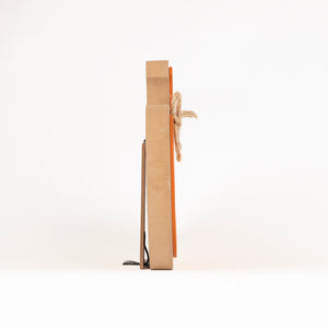 A minimalist wooden wall cross with a natural brown wood grain finish, featuring a rustic jute rope tied around the center and a small black metal footrest at the base, shown from a side profile view on a white background.