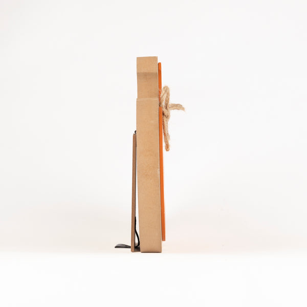 A minimalist wooden wall cross with a natural brown wood grain finish, featuring a rustic jute rope tied around the center and a small black metal footrest at the base, shown from a side profile view on a white background.