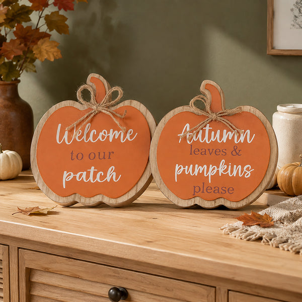 Two decorative pumpkin-shaped wooden signs with orange fronts and natural wood edges, placed on a wooden cabinet in a fall-themed room. One sign reads 'Welcome to our patch' and the other reads 'Autumn leaves & pumpkins please'.