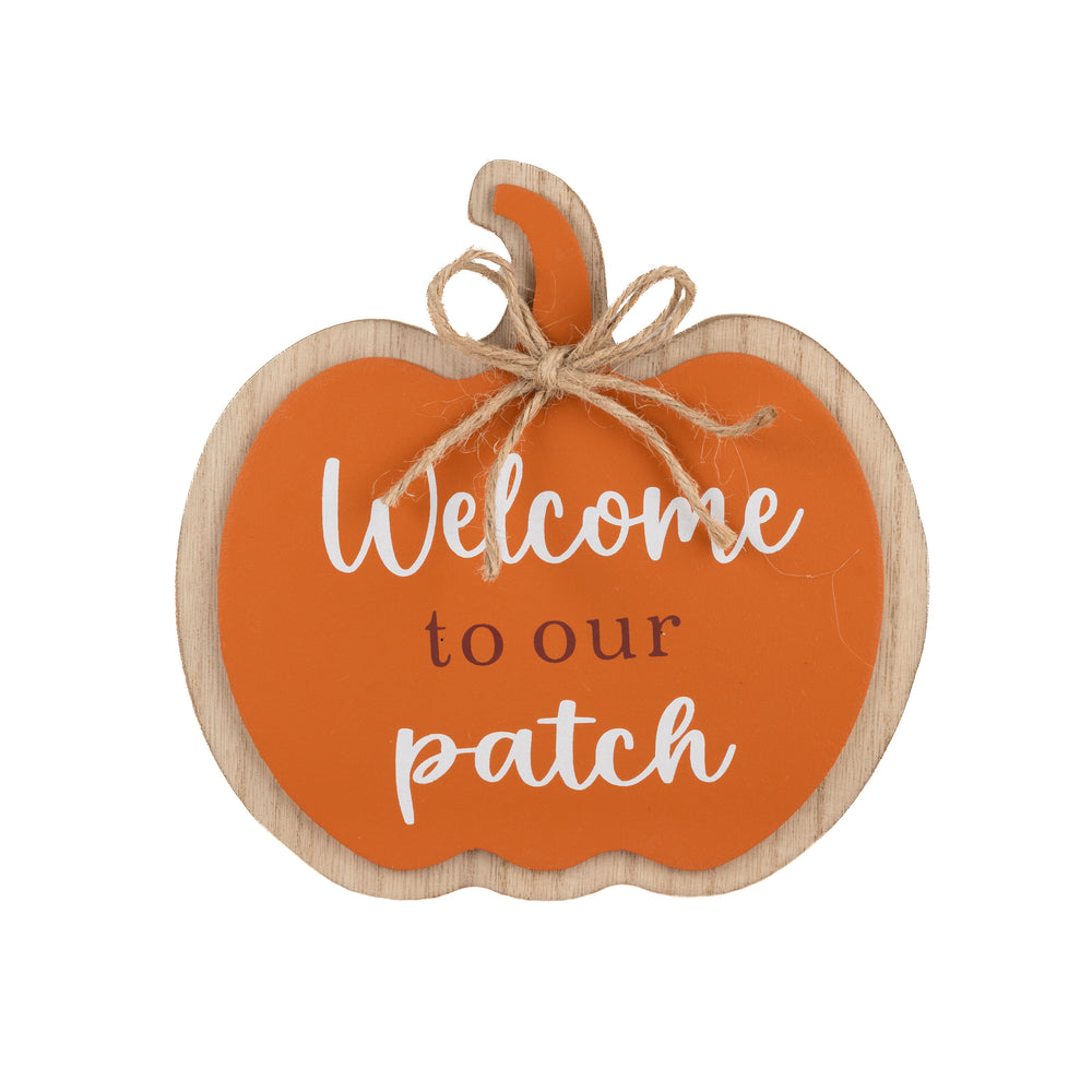 An autumn-themed wooden pumpkin sign with the text 'Welcome to our patch' in white and black lettering, styled on a fireplace mantel with a small orange pumpkin, a ceramic vase with fall leaves, and a lit candle.