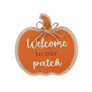 A decorative pumpkin-shaped wooden sign with an orange center, white script text reading 'Welcome to our patch,' brown lettering in the middle, and natural wood edges. A small piece of twine is tied around the top stem area.