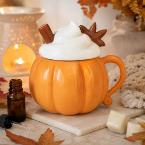 Orange pumpkin ceramic mug with whipped cream, cinnamon sticks and star anise, styled with autumn leaves and candles.