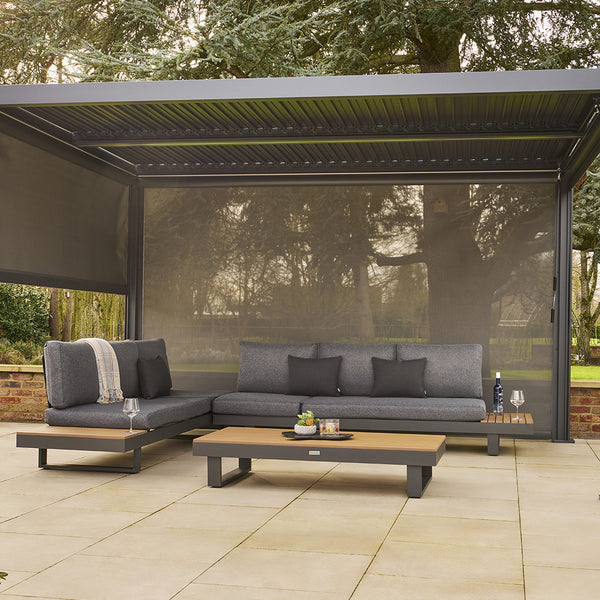 Outdoor patio with gray sectional sofa, coffee table, and pergola in a garden setting.