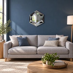 A modern gray fabric sofa in a styled living room with a dark blue wall, an octagonal geometric mirror, and decorative pillows.