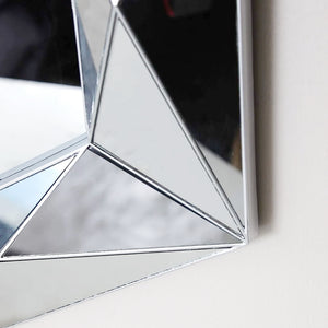 A close-up of a geometric star-shaped wall mirror with a polished silver frame, reflecting a neutral interior background.