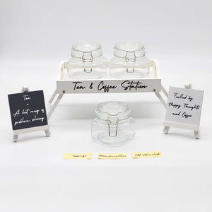 Tea and coffee station setup with glass jars and decorative signs on a white background