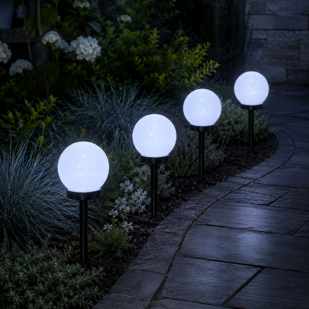 Four glowing spherical solar garden lights mounted on black stakes along a stone walkway in a landscaped garden at night.