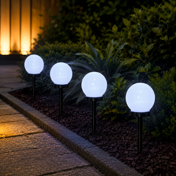 Four glowing spherical solar garden lights mounted on black stakes along a stone walkway in a landscaped garden at night.