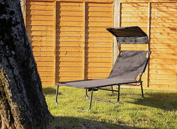 Gray lounge chair with canopy in a garden setting against a wooden fence.