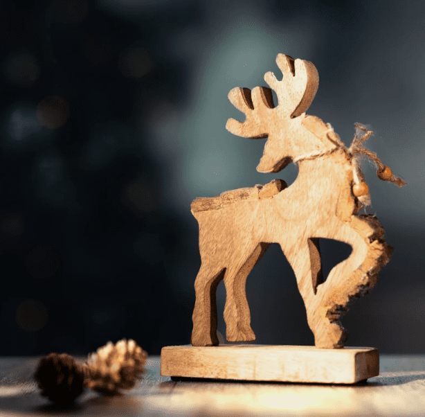 A wooden reindeer Christmas ornament placed on a surface with a blurred background, illuminated by a warm light.