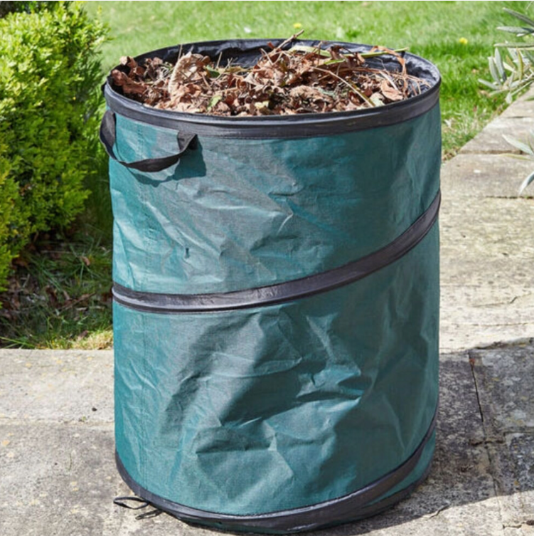 Green garden waste bag filled with leaves on a stone surface outdoors.