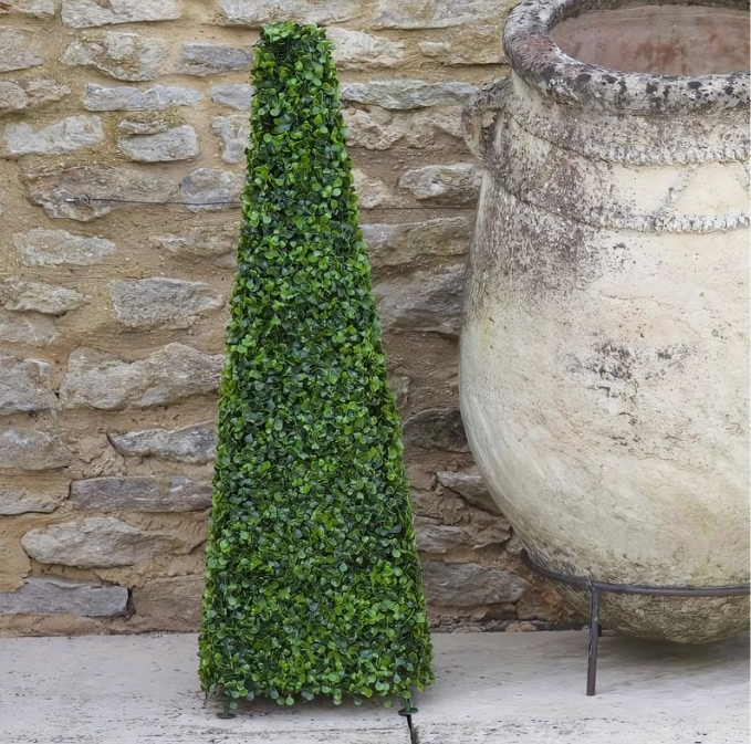 Tall green artificial topiary against a stone wall