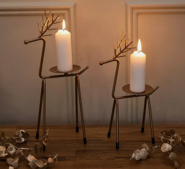 Two decorative reindeer candle holders with lit candles on a wooden surface.
