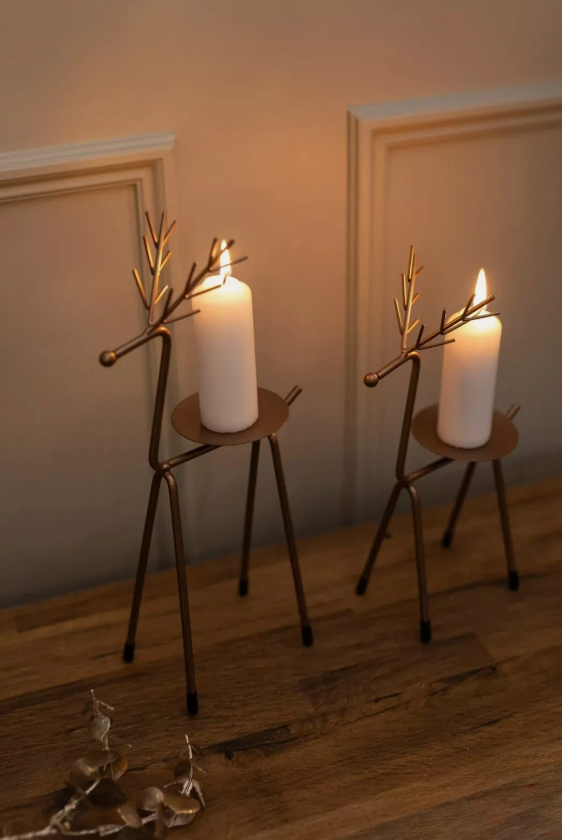 Two candle holders shaped like deer with lit candles on a wooden surface.