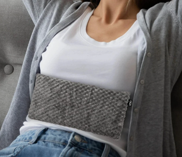 Person wearing a gray heating pad on their waist with a white shirt and blue jeans.
