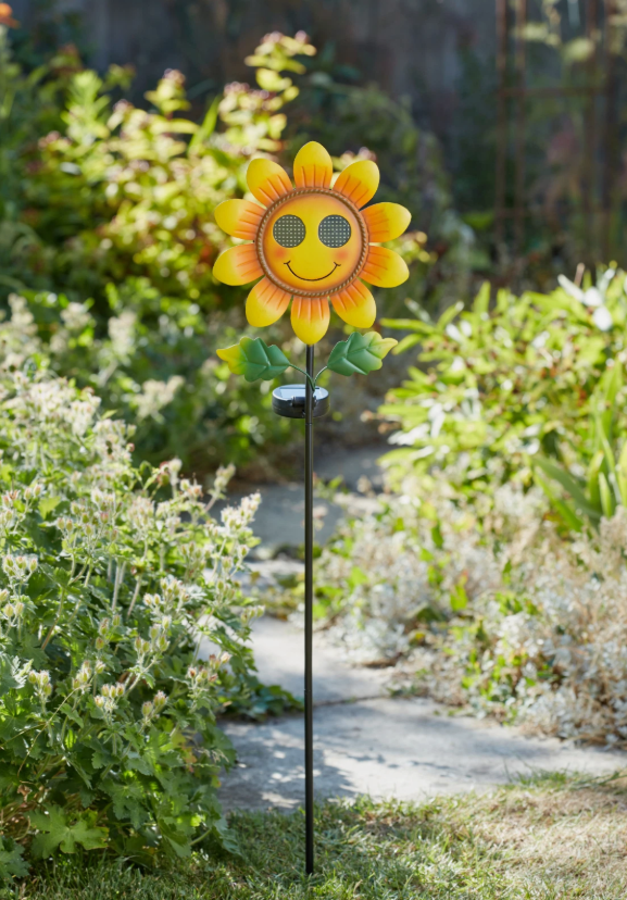 Sunflower-shaped garden stake with a smiley face in a garden setting