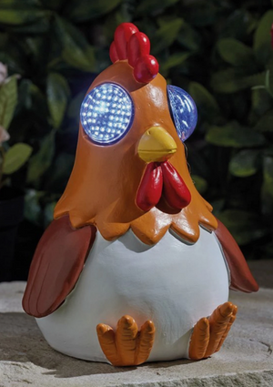 Solar-powered chicken figurine with LED eyes on a stone surface.