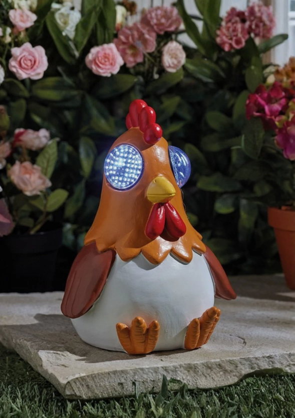 Decorative rooster with solar lights on a stone surface with flowers in the background