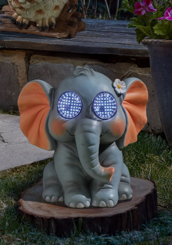 Decorative elephant figurine with glowing eyes on a wooden base outdoors.
