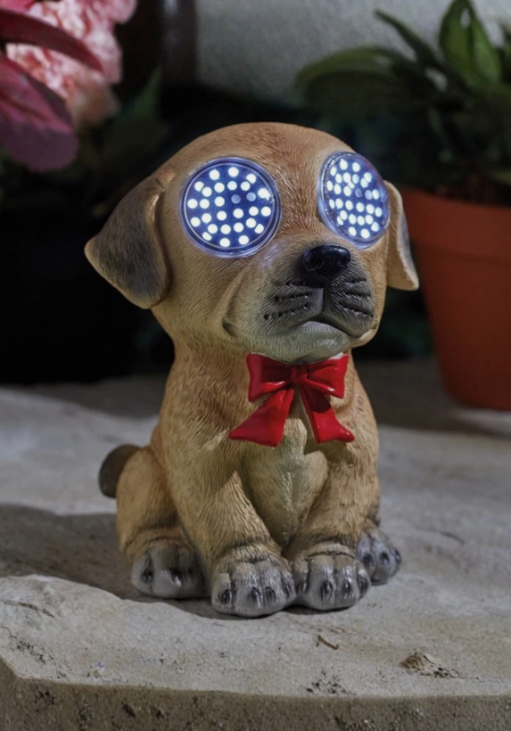 Dog figurine with LED eyes and a red bow tie on a stone surface.