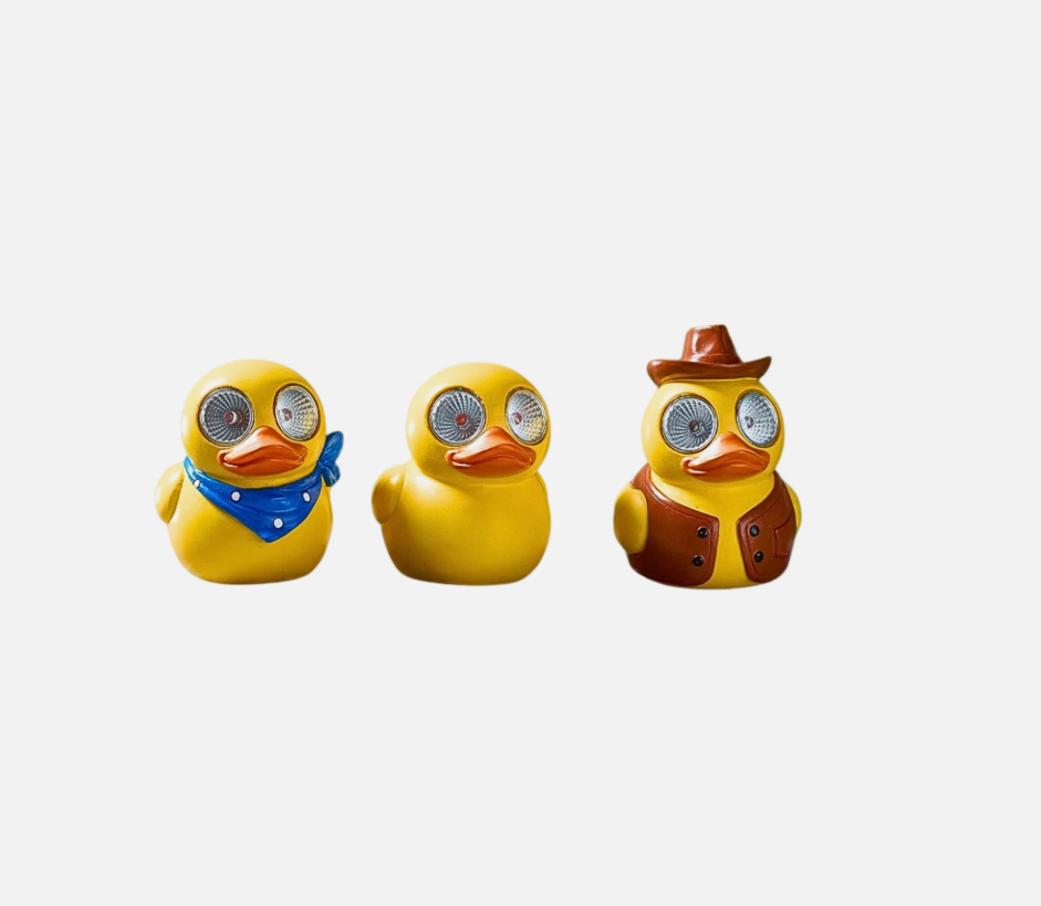 Three yellow rubber duck toys with different accessories on a surface with a blurred natural background.