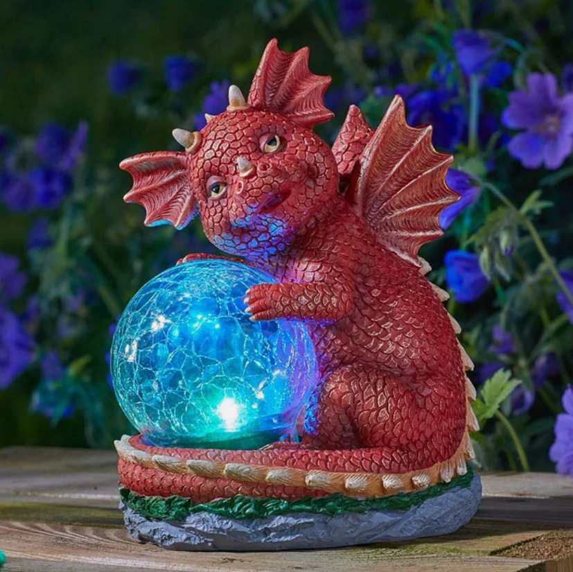 Decorative red dragon figurine holding a glowing blue crystal ball with a blurred floral background.