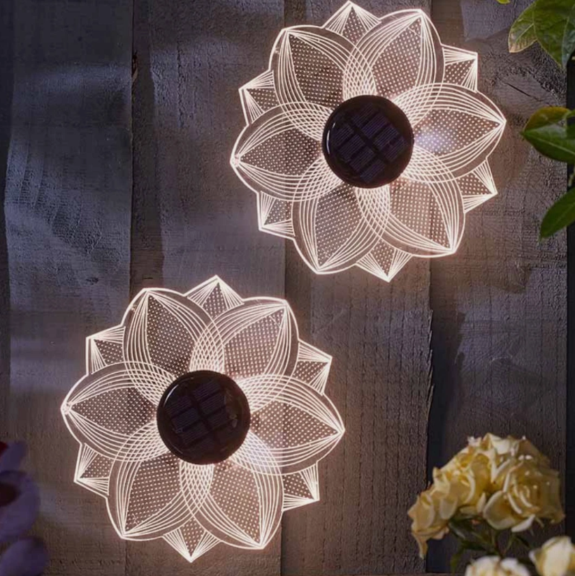 Two floral-patterned solar lights on a wooden surface with a plant in the background.