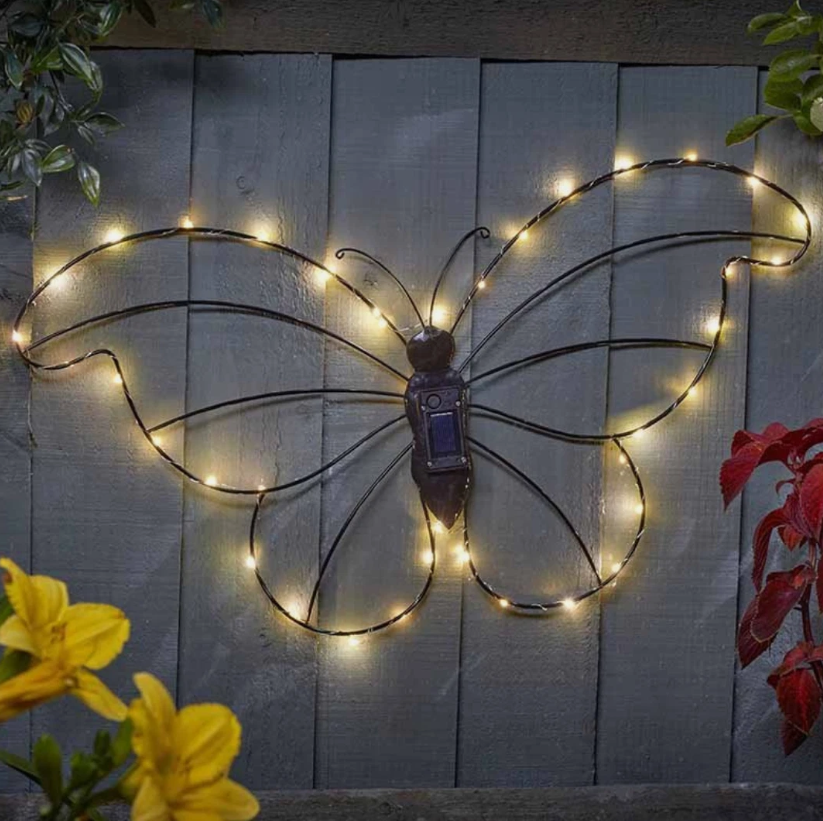 Decorative butterfly wall art with string lights on a wooden fence